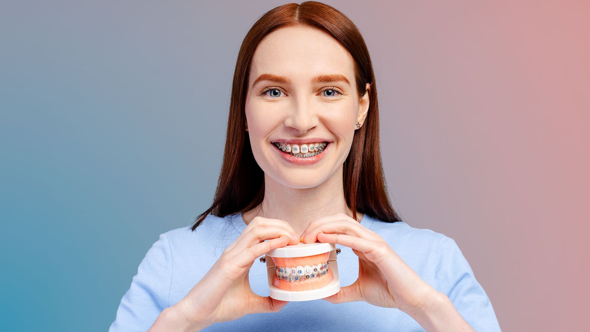 Braketli gülümseyen genç kadın, elinde renkli braket takılı çene modeli tutuyor