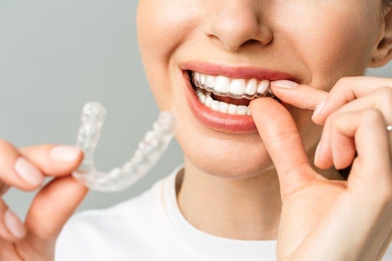 Kadın bir eliyle şeffaf plağı tutarken diğeriyle takılı plağı dudağından gösteriyor
